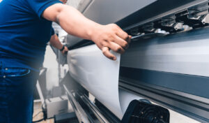 man holding printable material on alarge format printing plotter.